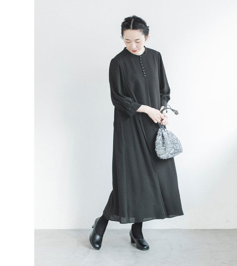黒のボタン付きワンピースを着た人物がシルバーの巾着バッグを持って立つ斜め前のコーディネート