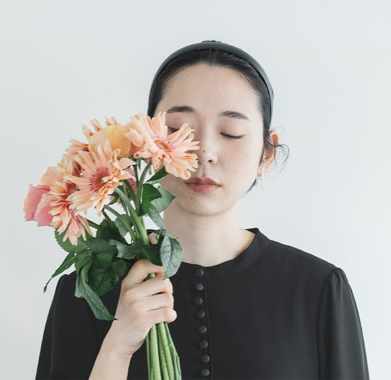 黒のボタン付きワンピースを着た人物が花束を顔に近づけて目を閉じているコーディネートカット