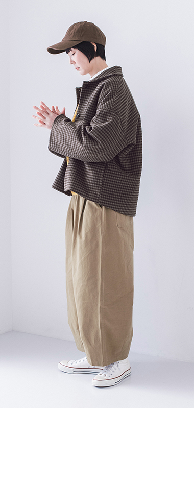 チェックジャケットとベージュパンツを着た人物の横姿、リラックスしたポーズ