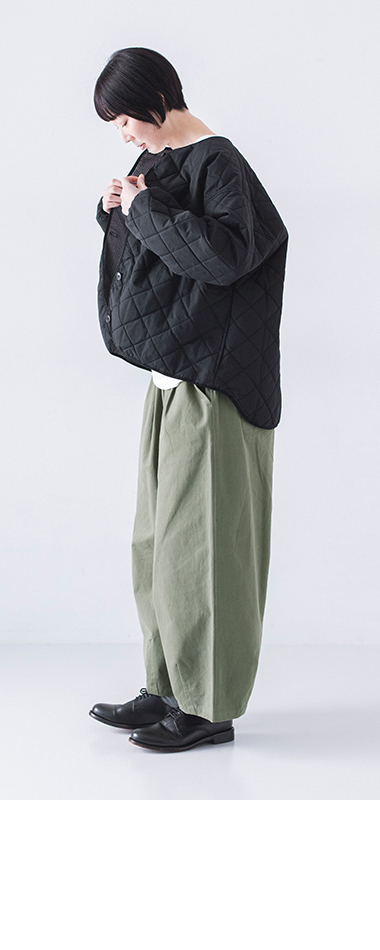 ブラックのキルティングジャケットを両手で整える横姿、モスグリーンパンツとのレイヤードスタイル
