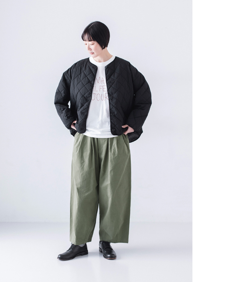 モスグリーンのワイドパンツと白Tシャツ、ブラックジャケットを着た人物が視線を落とすポーズ