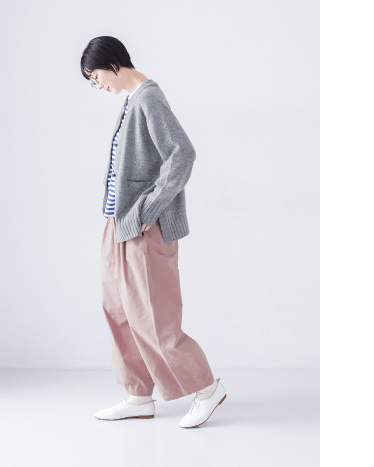  グレーのカーディガンとピンクパンツを着た人物の横姿、メガネをかけてうつむくポーズ