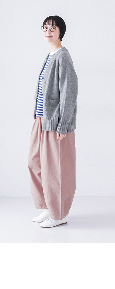 ピンクパンツとボーダーシャツを着た人物がメガネに手を添えて微笑むポーズ