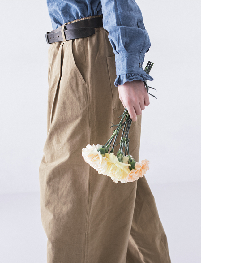 フリル襟のブルーシャツとベージュパンツ、手に持った花束が印象的な下半身アップ