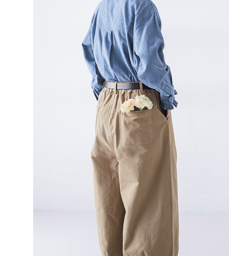 ベージュパンツの後ろポケットに花を挿した後ろ姿、ブルーシャツとのナチュラルなコーディネート