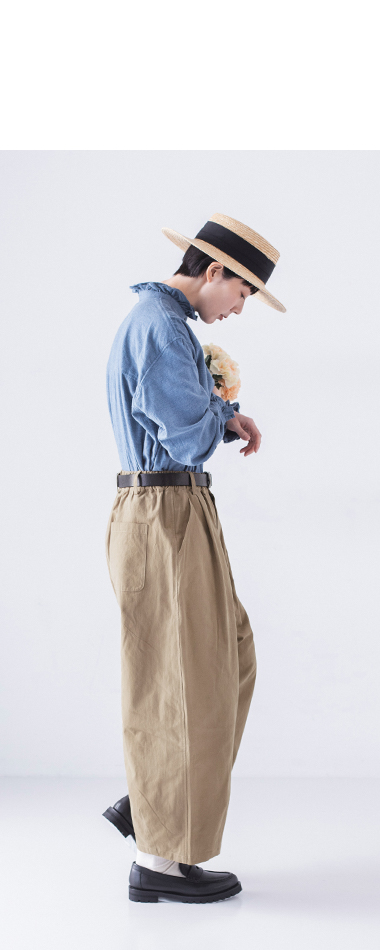 ストローハットをかぶり、花束を見つめる横姿のコーディネート、ブルーシャツとベージュパンツの組み合わせ
