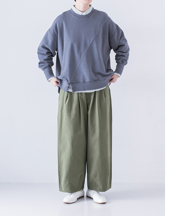 ストライプシャツをのぞかせたブルースウェットとモスグリーンパンツのコーディネート、手を腰に添えたポーズ