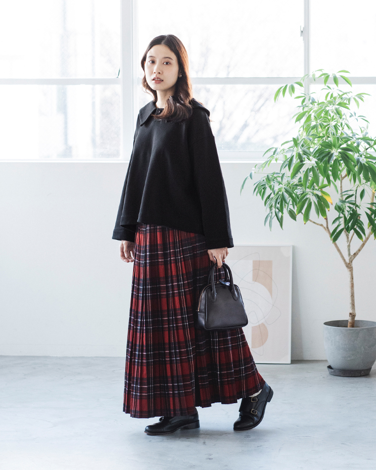 ブラックのプルオーバーと赤×黒のチェック柄スカートを合わせたコーディネート（室内・観葉植物とアートのある背景）