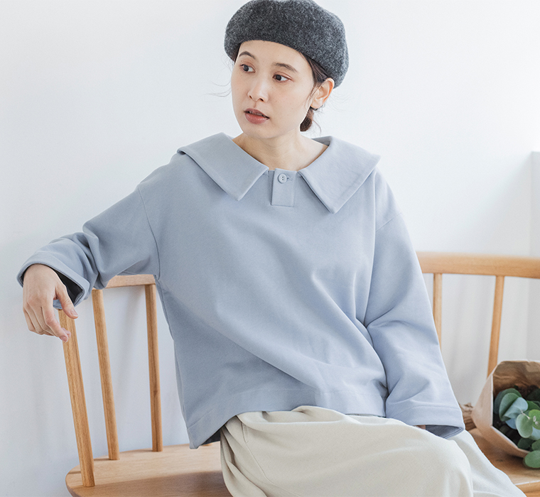 アイスブルーのプルオーバーとグレーのベレー帽を着用した人物が木製ベンチに座るコーディネート（花束付き）