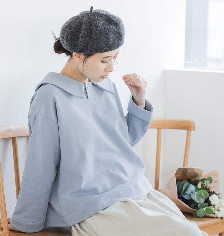 アイスブルーのプルオーバーとグレーのベレー帽を着用した人物が木製ベンチに座るコーディネート（花束付き）
