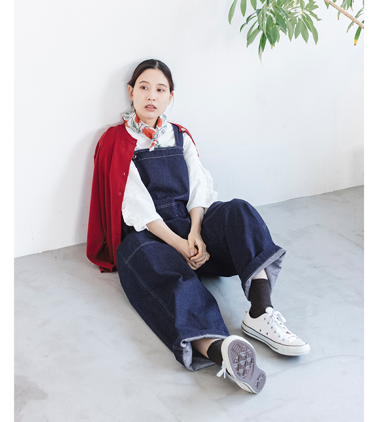 デニムオーバーオールに赤いカーディガンを肩掛けした座りポーズのコーディネート