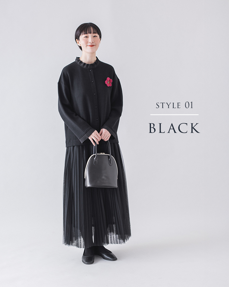 ピンクの花ブローチをアクセントにしたブラックコーディネートの全身スタイル（プリーツスカート・黒タイツ・黒バッグ）