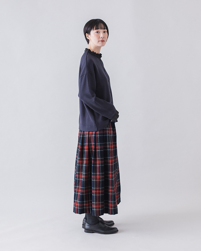 ネイビーのカーディガンと赤系チェック柄プリーツスカートを合わせた横向きコーディネート（黒のレースアップシューズ）