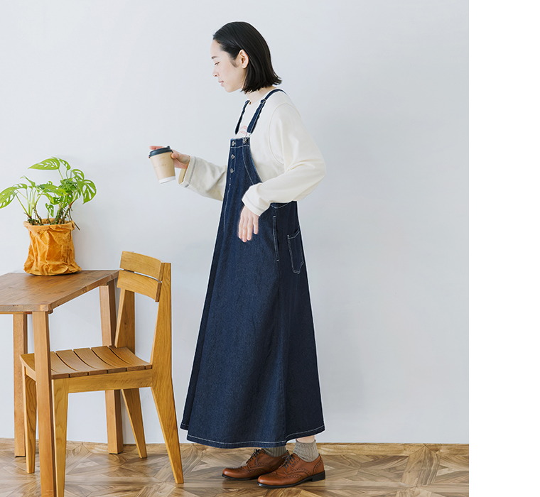 ワークジャンパースカートを着用しカップを持って横向きに立つ全身