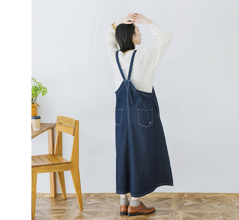 ワークジャンパースカートを着用し後ろ向きで両腕を上げた全身