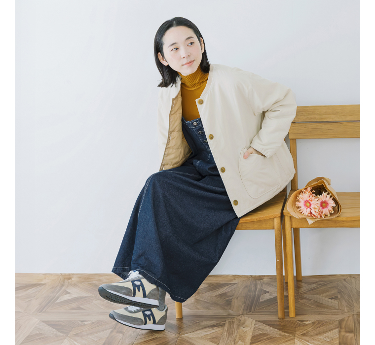 ワークジャンパースカートにアウターを重ねて椅子に腰掛けた全身