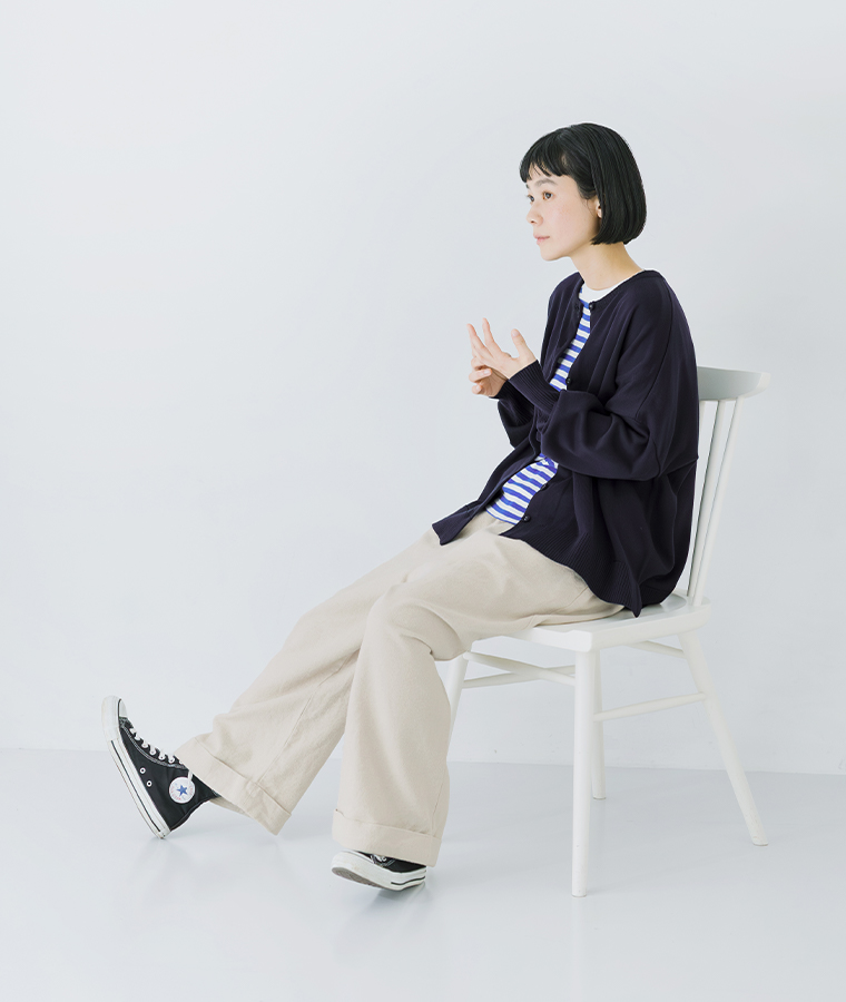 ネイビーのカーディガンをボーダーシャツとパンツに合わせたコーディネート（椅子に座るポーズ）