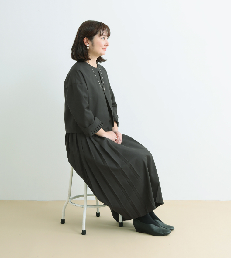 スタッフ身長159cmがジャケットプリーツアンサンブル（ブラックMサイズ）を着用し椅子にすわったカット