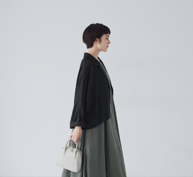 ブラックのショートテーラードジャケットとカーキのワンピースを着た横向きのコーディネート