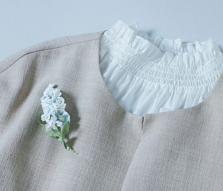 淡色トップスに淡いブルーの布花アクセサリーを合わせた胸元の着用イメージ
