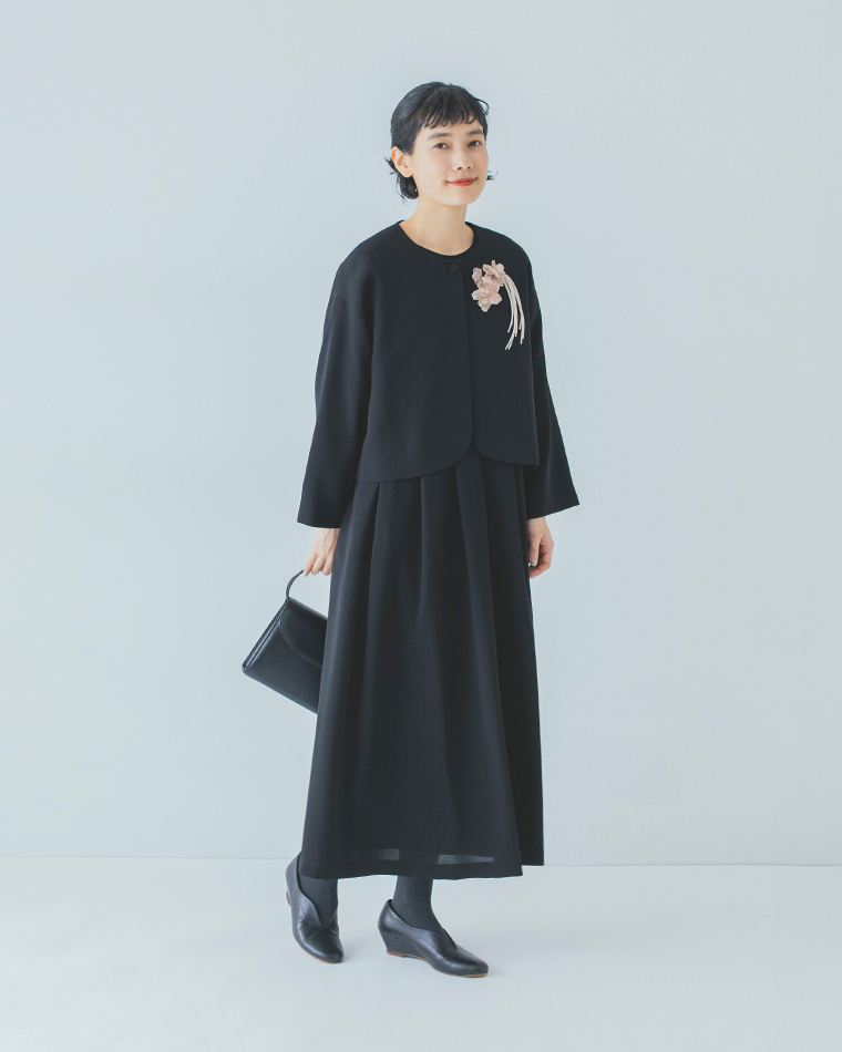 黒いフォーマルワンピースとジャケットに淡いピンクの布花コサージュを合わせた全身コーディネート
