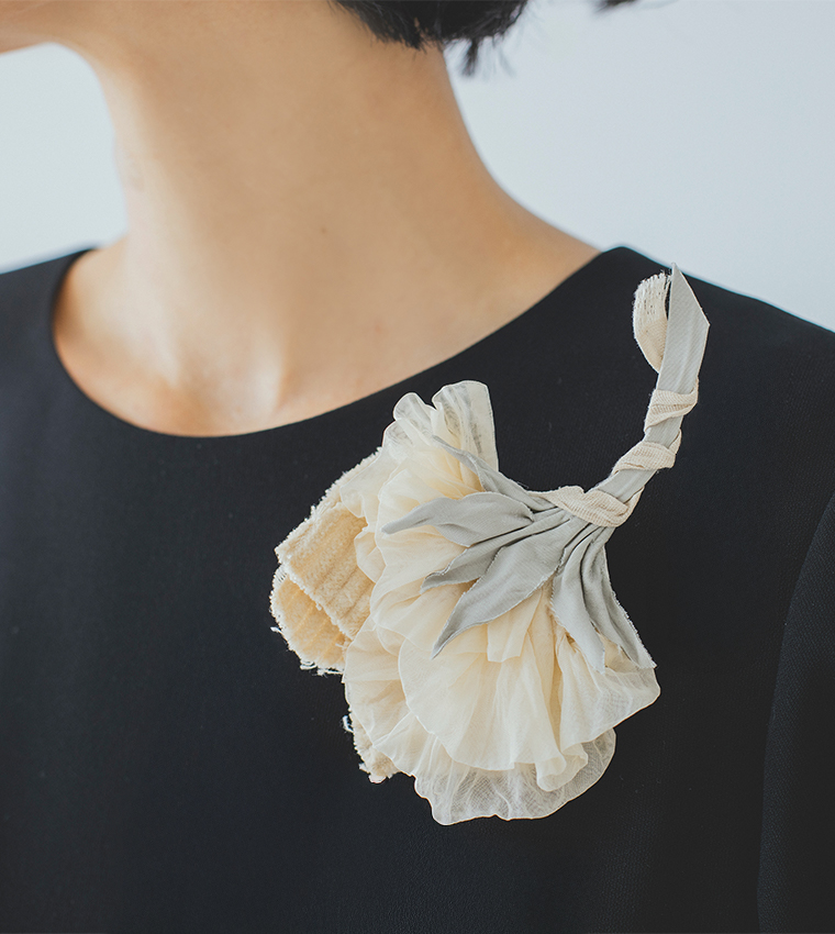 黒いワンピースに淡いクリーム系の布花コサージュを合わせた肩元のディテールカット