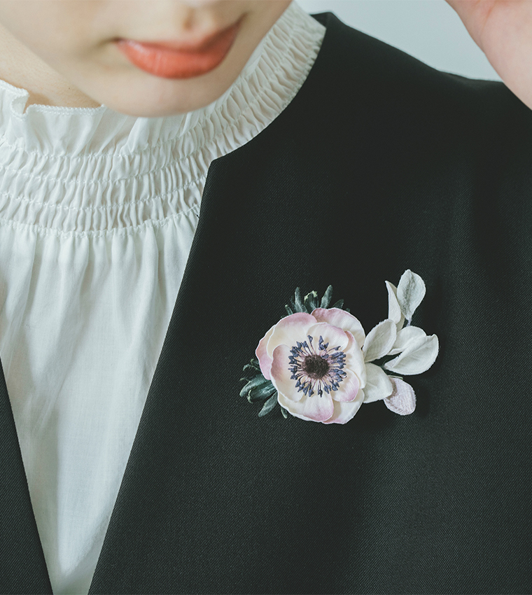 黒いジャケットにピンクと白の布花コサージュを合わせた胸元のディテールカット