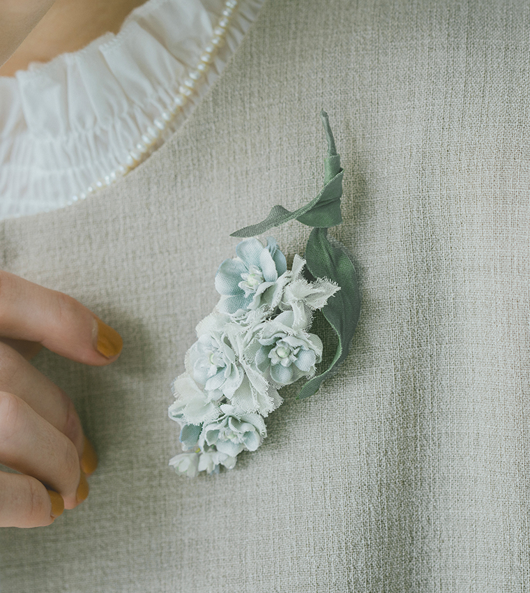 淡いブルーとホワイトの布花コサージュをライトベージュのジャケットに合わせた胸元のディテールカット