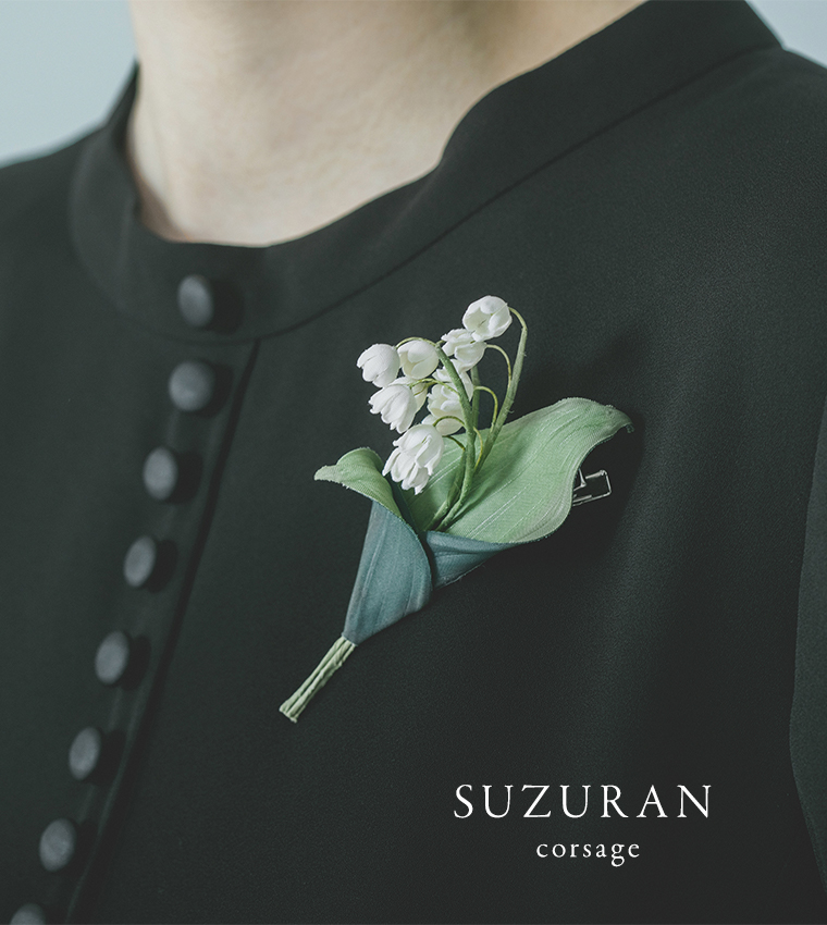 黒いワンピースにスズラン風コサージュを合わせた胸元のディテールカット