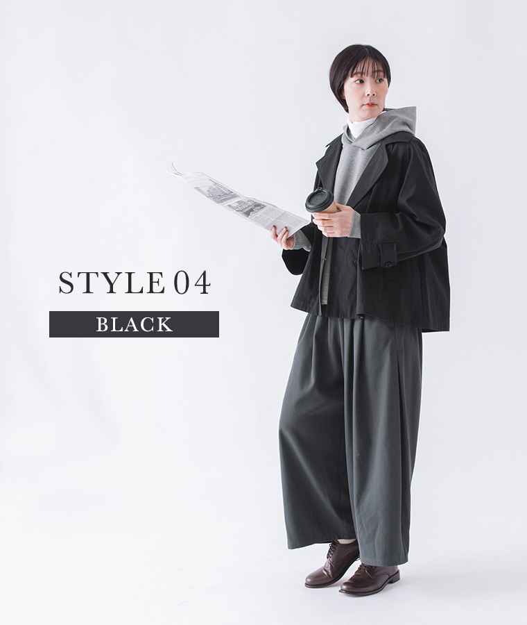 コットンナイロン ダブルボタンジャケットのブラックをフード付きトップスとワイドパンツに合わせて新聞とカップを持ったコーディネートカット