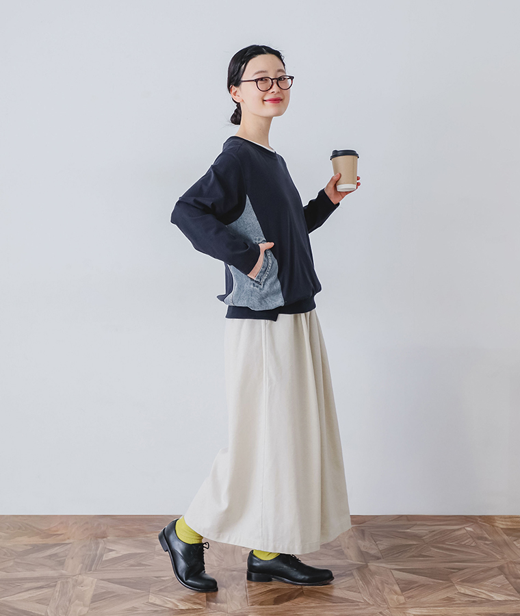 デニム切替プルオーバーを着用しサイドのデニム切替とポケットが見える横向きでカップを手に持ちロングスカートと革靴を合わせたコーディネートカット