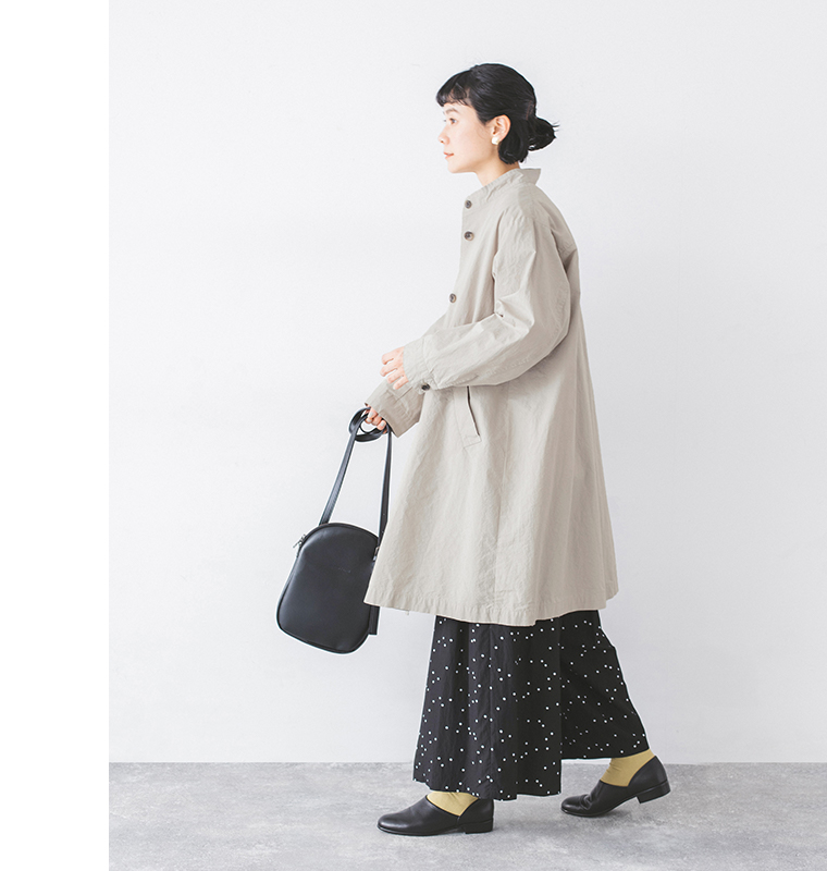 別注｜ハイネック比翼ミドル丈コートのグレーを着用した横向きのスタイルでドット柄スカートと黒いシューズとショルダーバッグを合わせたコーディネート
