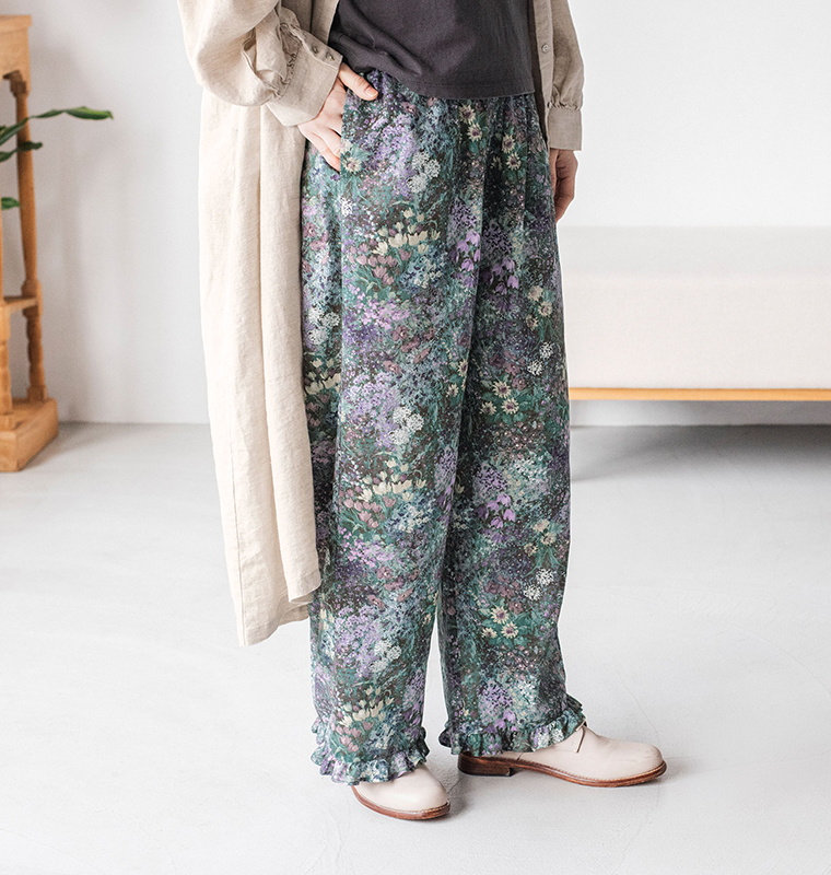 ベージュのロングワンピースに「PURPLE」カラーのフラワープリントパンツを合わせたコーディネート（白ソールのシューズを履いた室内スタイル）