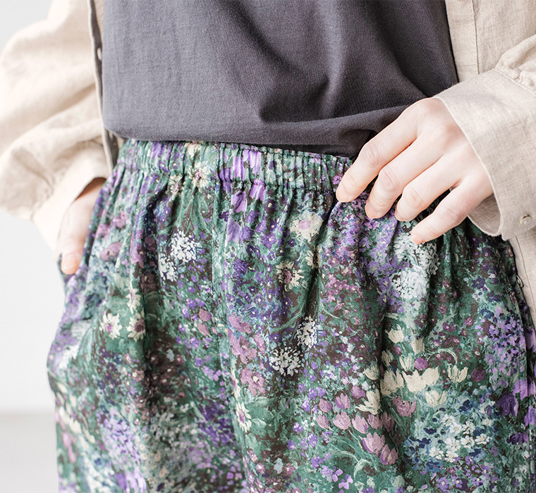 「PURPLE」カラーのフラワープリントパンツのウエストまわりディテール（ベージュのワンピースとダークグレーのトップスを合わせたスタイリング）