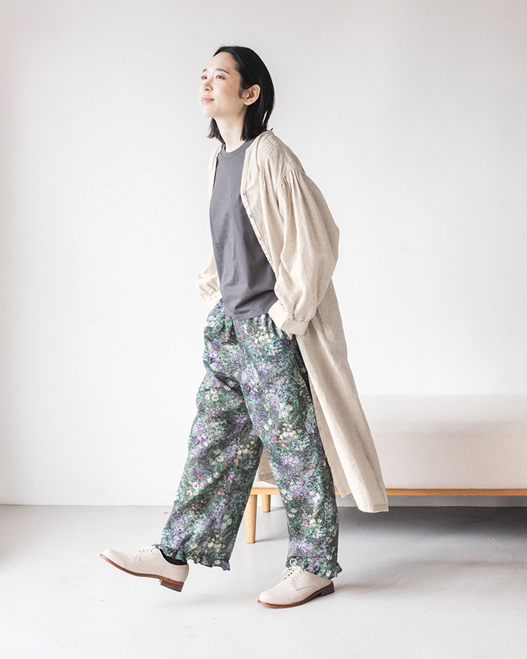 「PURPLE」カラーのフラワープリントパンツを主役にしたコーディネート（ベージュのワンピースとダークグレーのトップスを合わせたスタイリング）