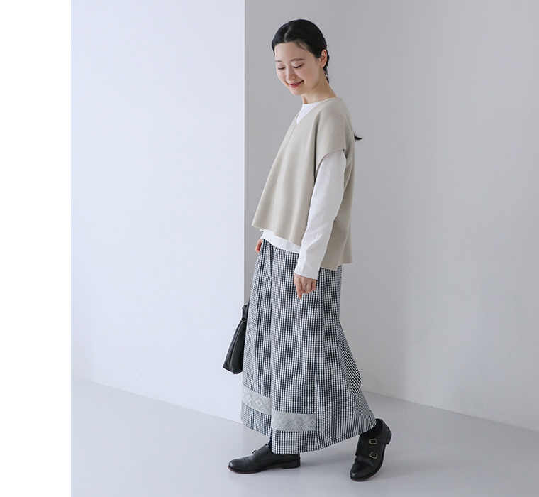 レース付きワイドパンツを着用しベージュのニットベストと白インナーを重ねたコーディネートで歩くカット