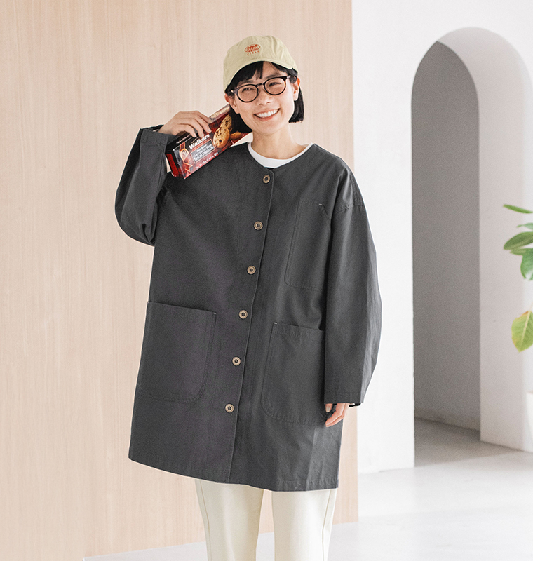 チャコールのライトコートを着た人物がマカダミアクッキーのパッケージを手に笑顔を見せるライフスタイルカット