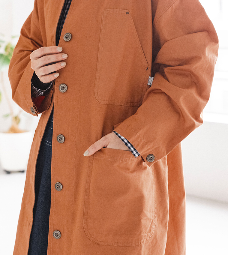 オレンジのライトコートのポケットのディテール画像（手をポケットに入れた着用カット）