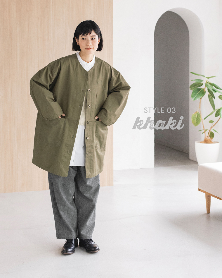 カーキのライトコートを使ったSTYLE 03の全身コーディネート（白シャツ・グレーパンツ・黒シューズ着用、室内観葉植物あり）