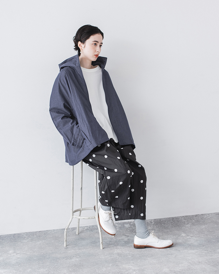 ネイビーのフード付きジップジャケットとドット柄ワイドパンツを着用し、白いスツールに腰掛けたスタイリングカット