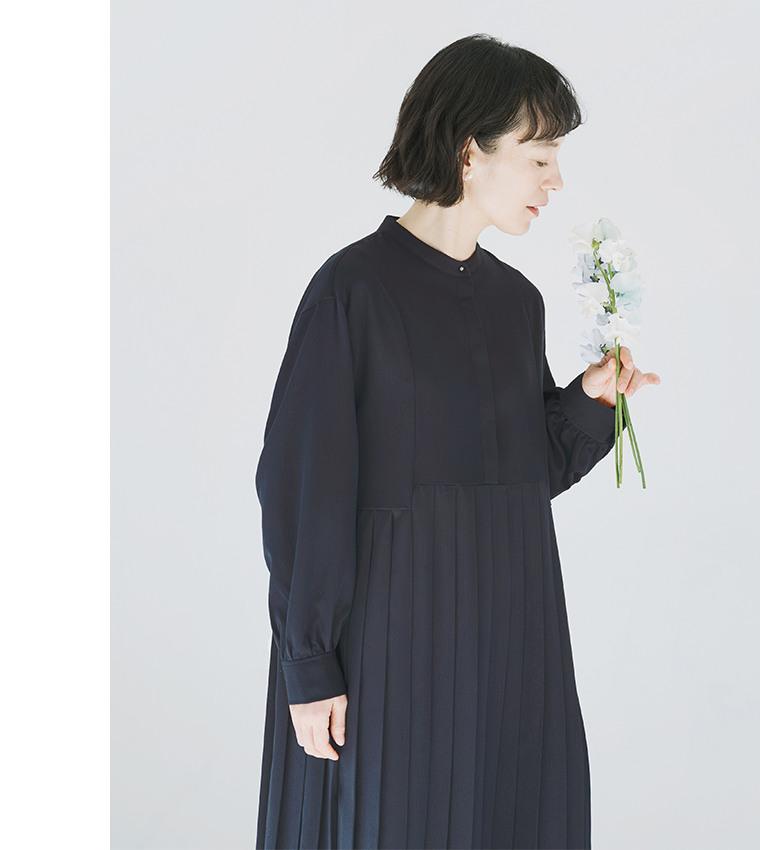 ネイビーのプリーツワンピースを着用し、白とブルーの花束を見つめる横向きのコーディネート