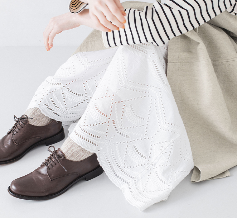 カットワークレースワイドパンツ(ホワイト)を着用して座って裾レースに寄ったカット