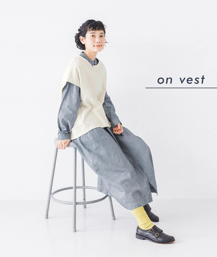 別注｜ヒッコリー ループ釦ワンピースを着用したモデルがスツールに座っている全身カット