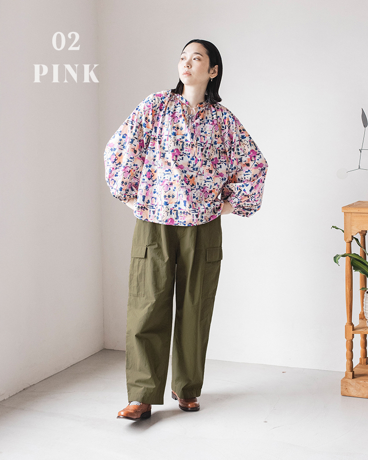 「02 PINK」と表示された白い壁の前で、ピンク・パープル系の抽象柄ブラウスとカーキのカーゴパンツを着た人物のコーディネート写真