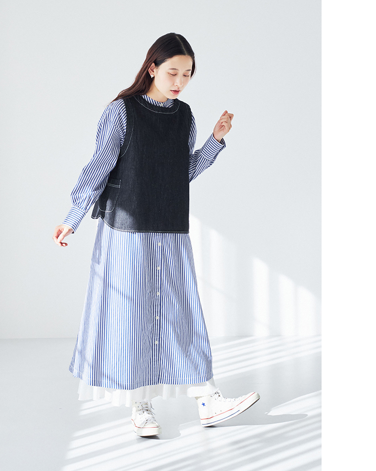 ストライプ柄シャツワンピースにデニムベストを重ね、白のハイカットスニーカーを合わせたコーディネート（室内・自然光・動きのあるポーズ）