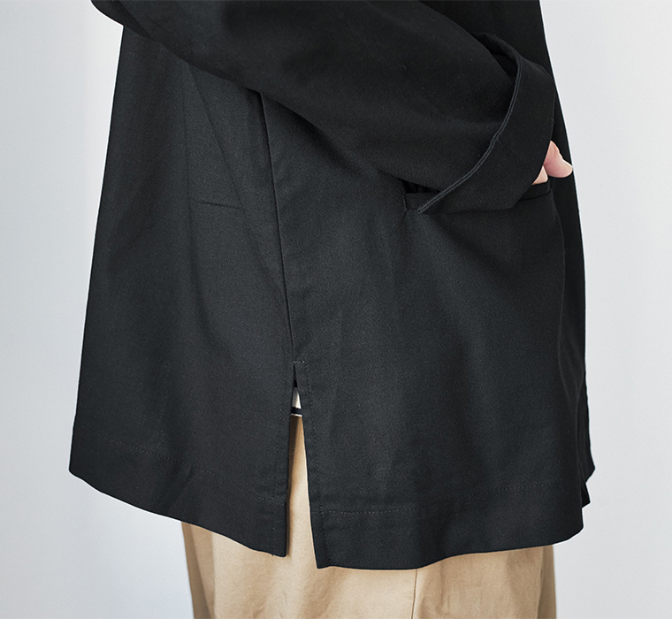 ブラックのジャケットとベージュパンツのサイドディテール（スリット入り・ポケットに手を入れた様子）