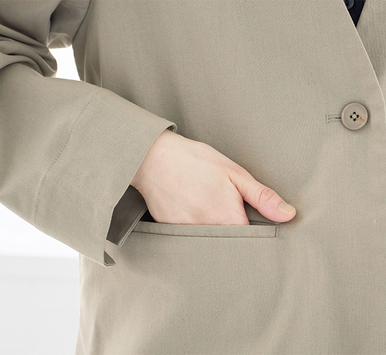 グレージュのジャケットのポケットに手を入れたディテールカット（フロントボタン・スリットポケット）