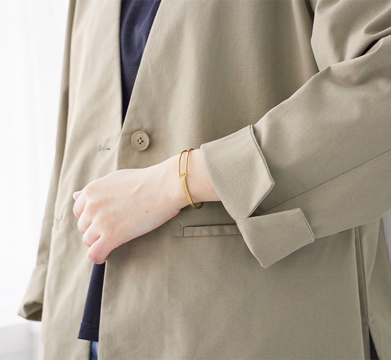グレージュのジャケットと黒トップスのディテールカット（ゴールドのミニマルブレスレット付き）