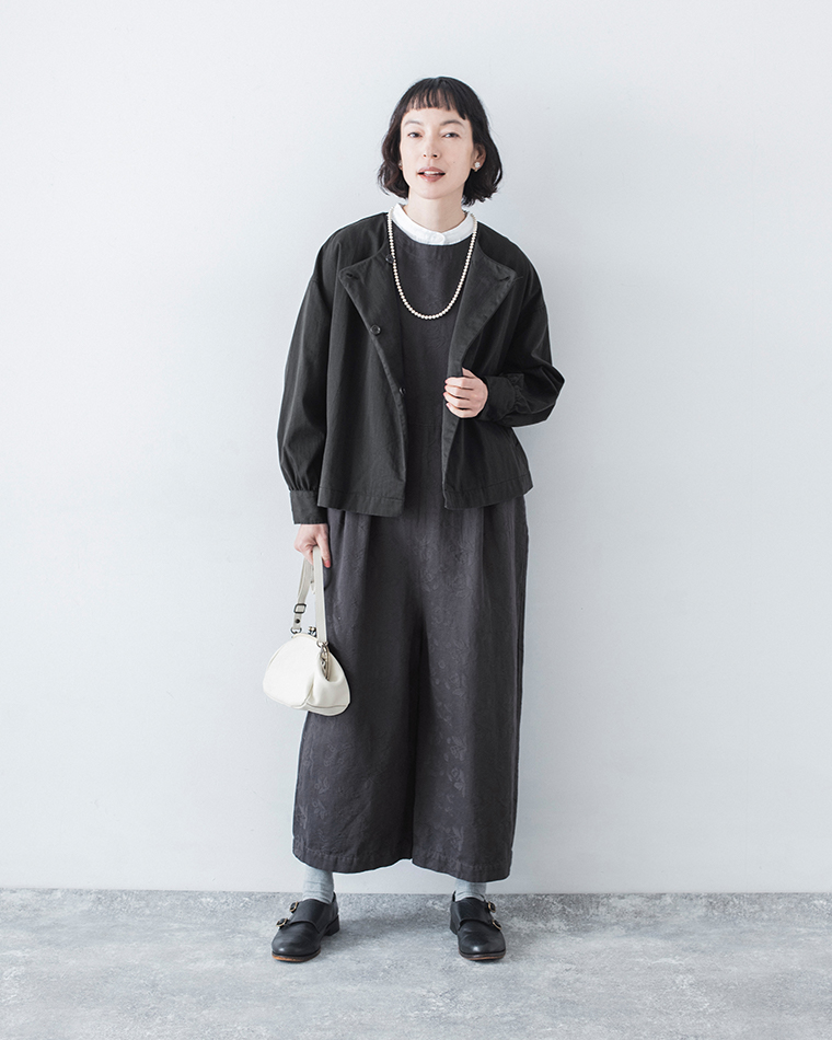 ャコールのジャカードオールインワンに黒ジャケットを重ね、白ブラウスと白バッグを合わせた全身コーディネート画像