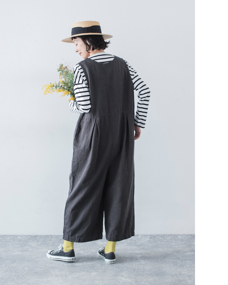 チャコールの2wayオールインワンをボーダーカットソーに重ね、花を手にした後ろ姿のコーディネート画像